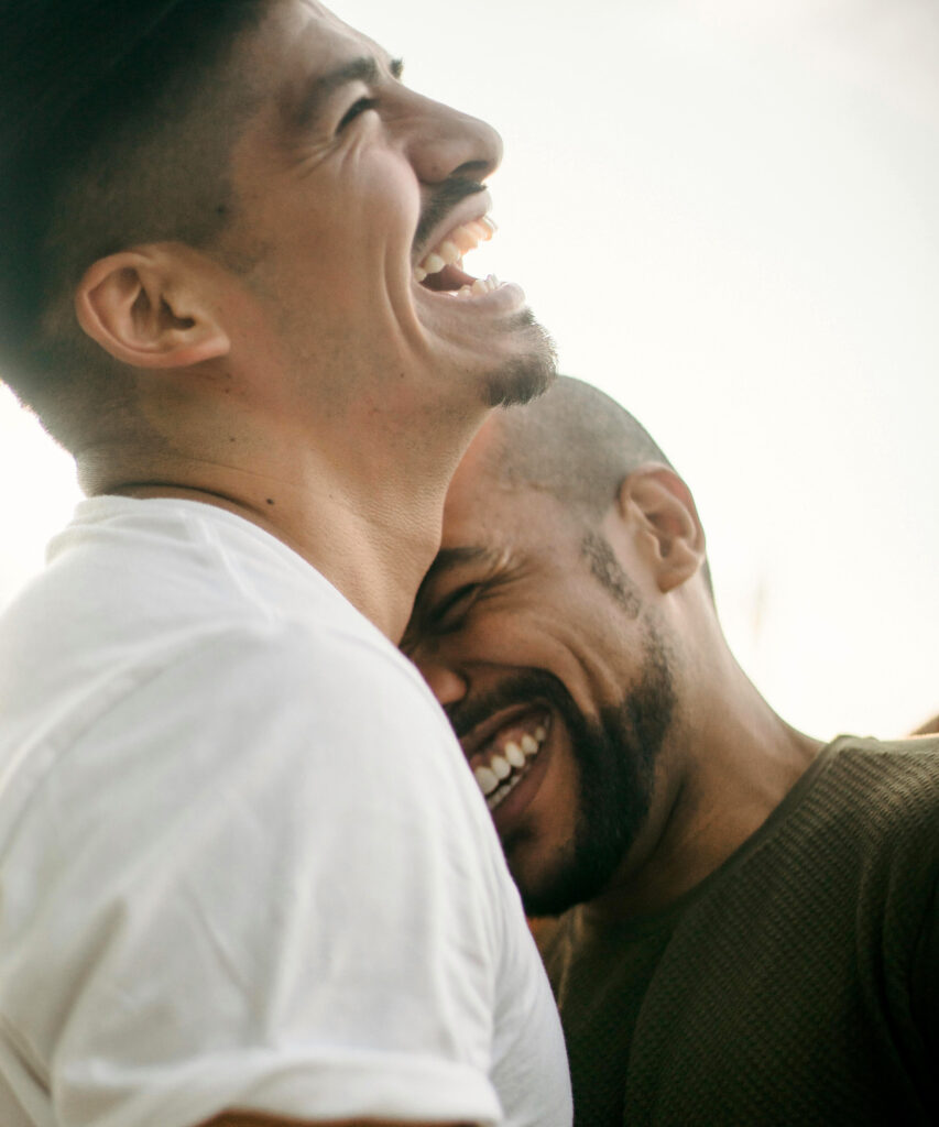 Two young men laugh and hug with genuine human love and intimacy