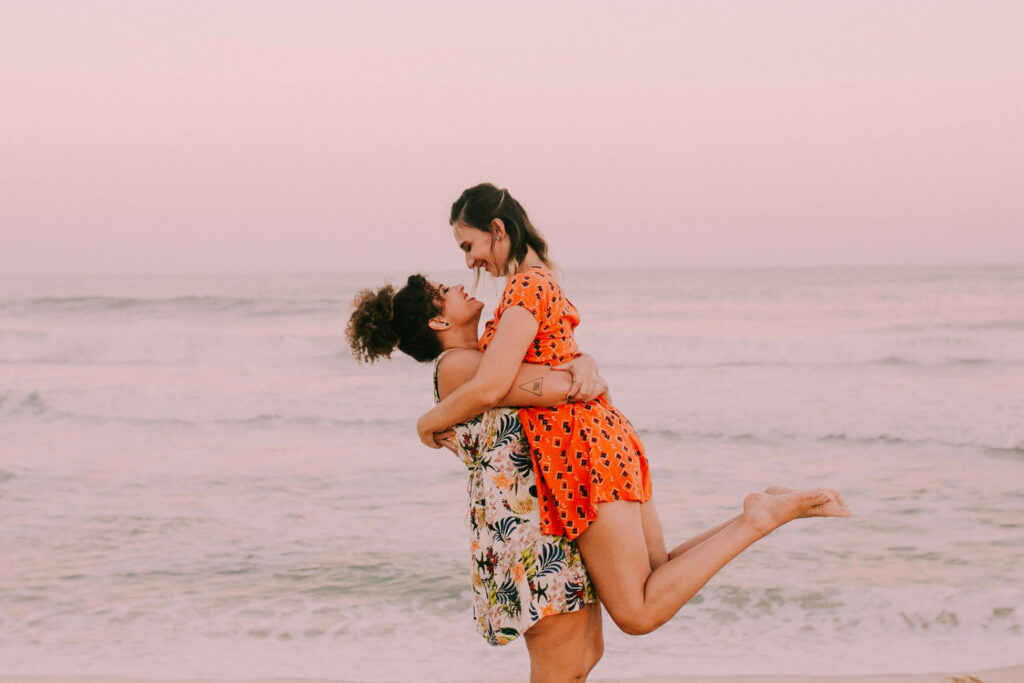 Couple on the beach, embracing and smiling, because they know how to be vulnerable