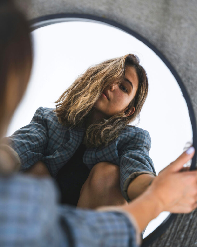Young woman, observing herself in a mirror, thinking about her self protection strategies